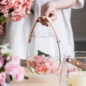 elegant glass vase lifestyle shot with pink flowers and a person holding the leather strap